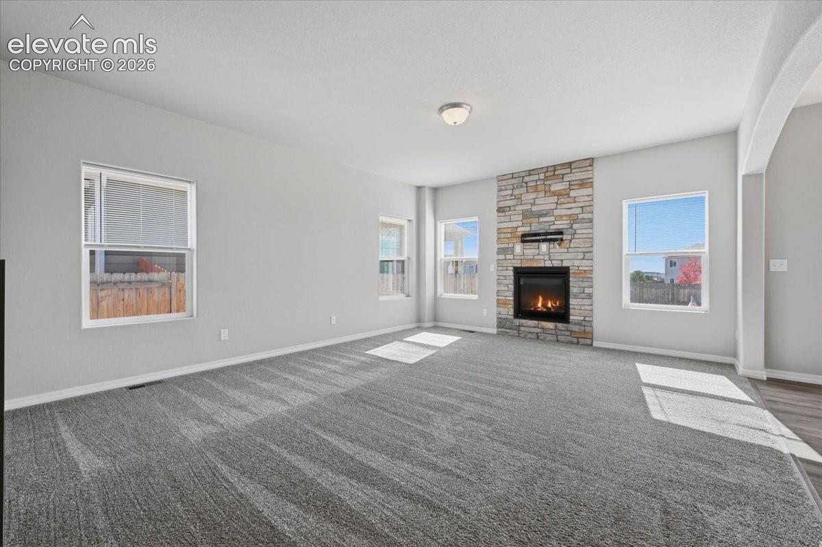 Living area featuring neutral wall tones, plush wall-to-wall carpeting, multiple windows, and a floor-to-ceiling stone-facade fireplace
