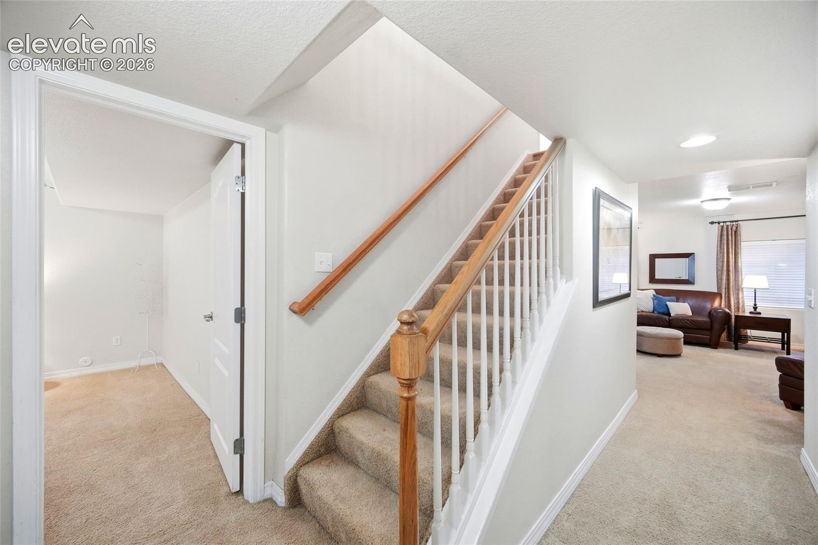 Carpeted staircase with wood handrail, white balusters, and recessed lighting