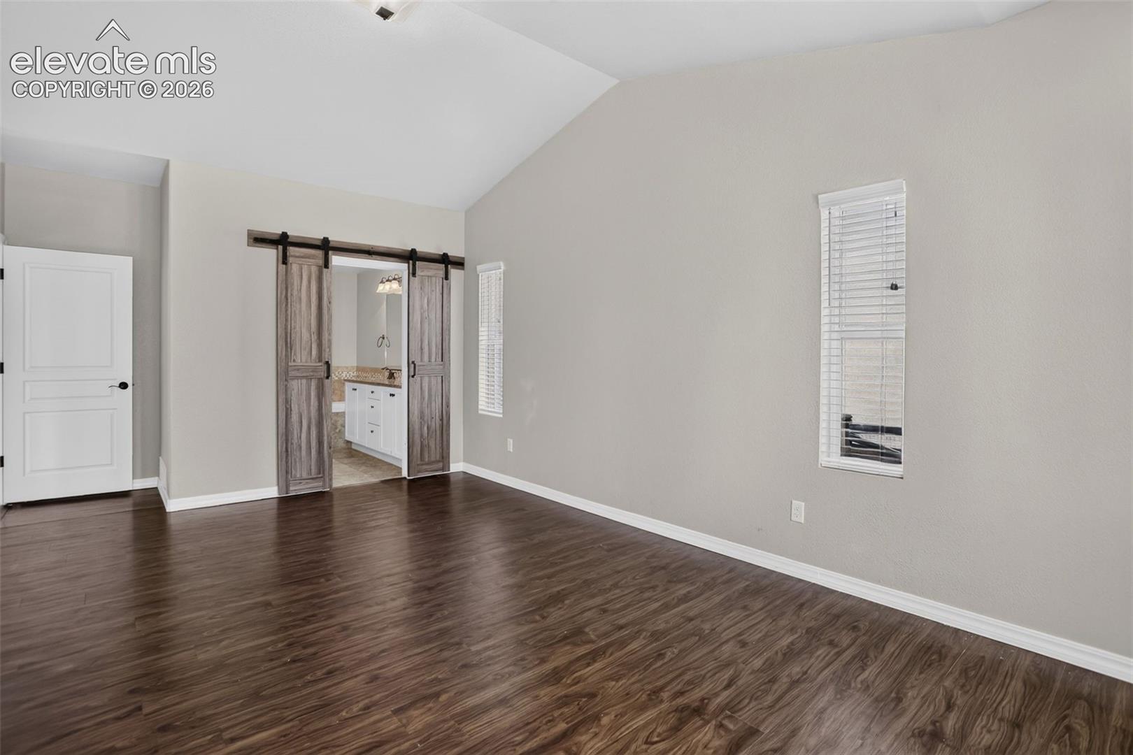 Vaulted ceiling, wood-finish flooring, and a white interior door