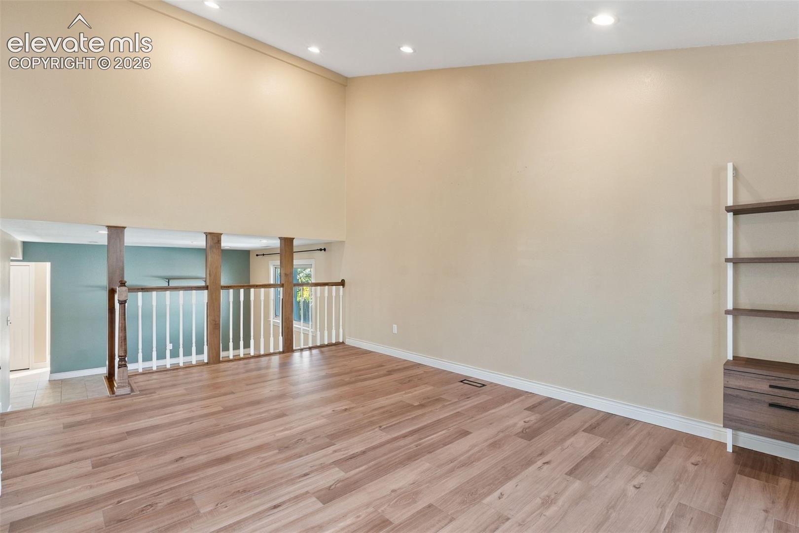 Vaulted ceilings, wood-finish flooring, recessed lighting, and a custom wood-railing partition featuring white spindles