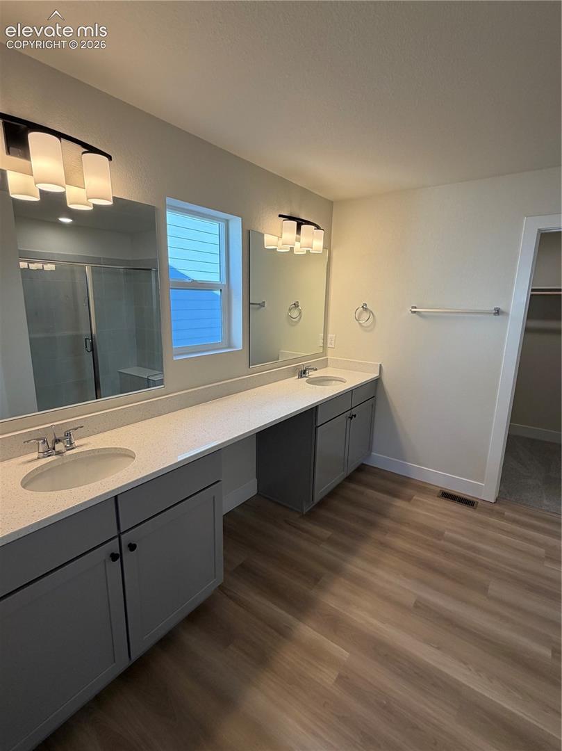 Dual-sink vanity with light-tone solid surface countertops, grey cabinetry, integrated mirrors, and wood-finish flooring