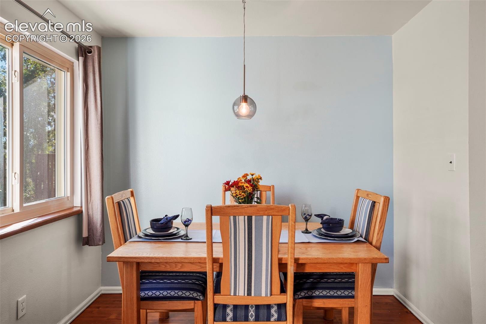 Dining area featuring wood-finish flooring, a light-filled window with a wood-finished sill, a minimalist spherical pendant light, and a dedicated accent wall