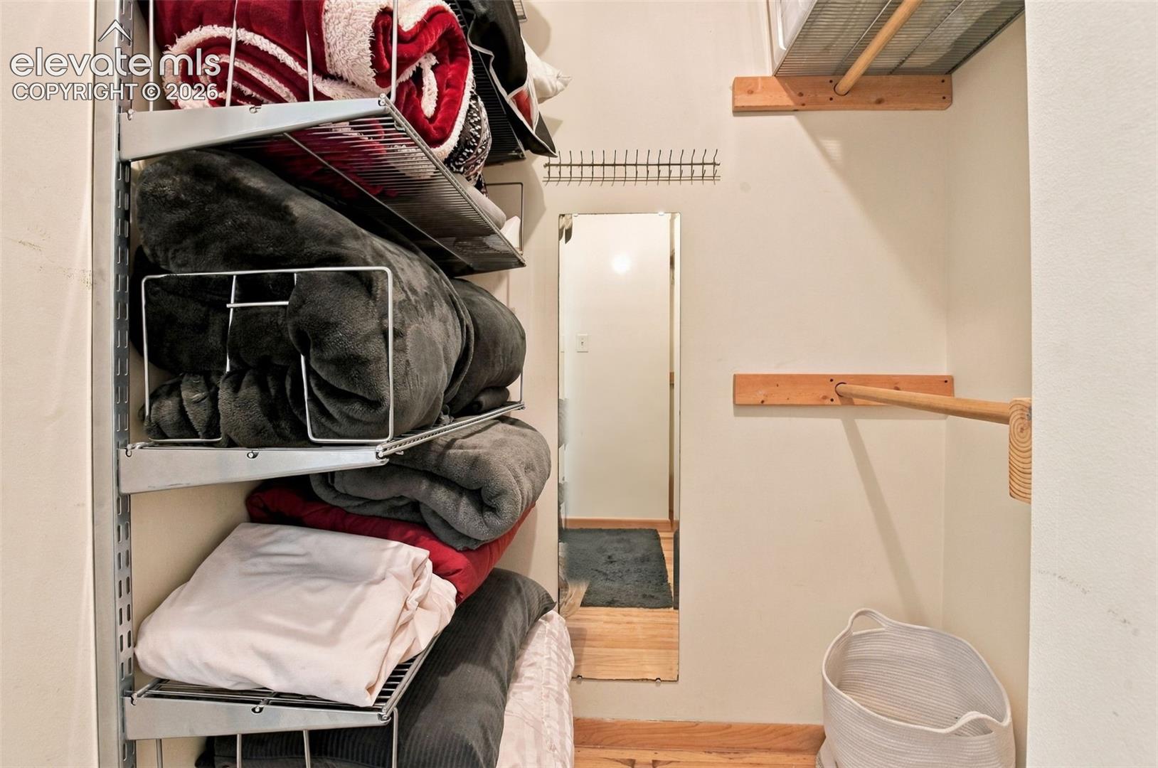 Walk-in storage space featuring adjustable wire shelving, integrated wood-finish clothing rods, and a full-length wall-mounted mirror