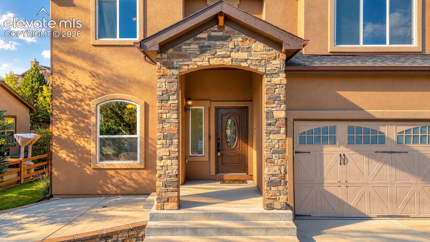 Stucco exterior with stone accents, covered entry, arched front door with oval glass insert, and a two-car garage with arched window panels