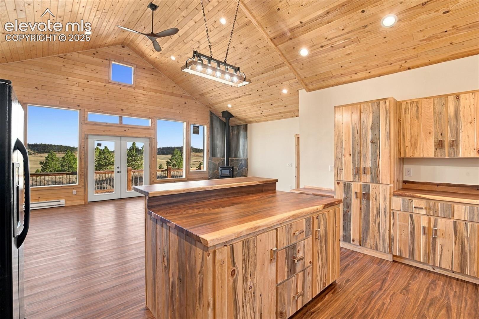 Vaulted wood-plank ceiling, natural finish wood cabinetry, live-edge wood kitchen island countertop, large-scale windows, and wood-finish flooring