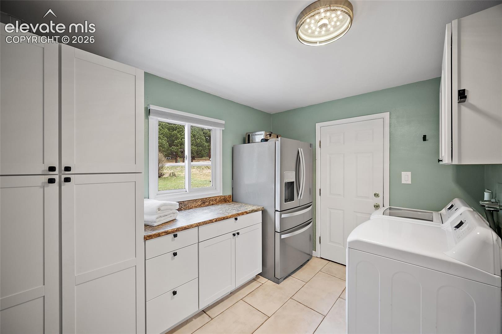 Laundry area featuring white shaker-style cabinetry, stone-finish countertops, tile flooring, and a flush-mount circular light fixture