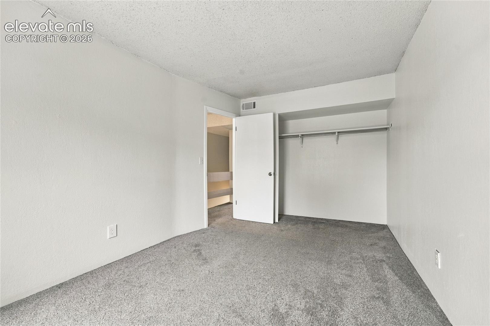 Interior space featuring neutral-toned carpeting, white walls, and a built-in closet with an overhead shelf