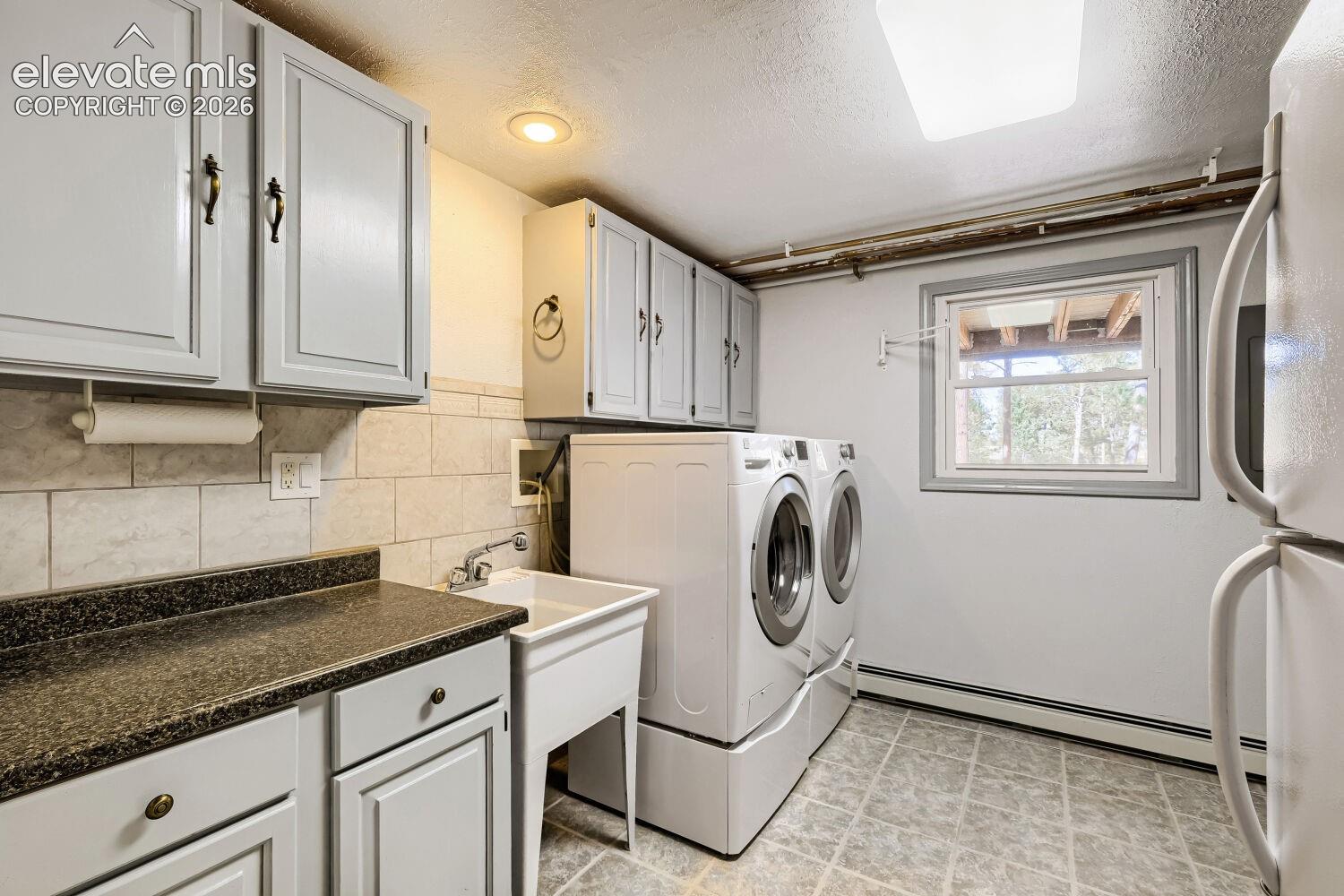 Laundry area featuring overhead and base cabinetry, a utility sink, a single window, and tiled flooring