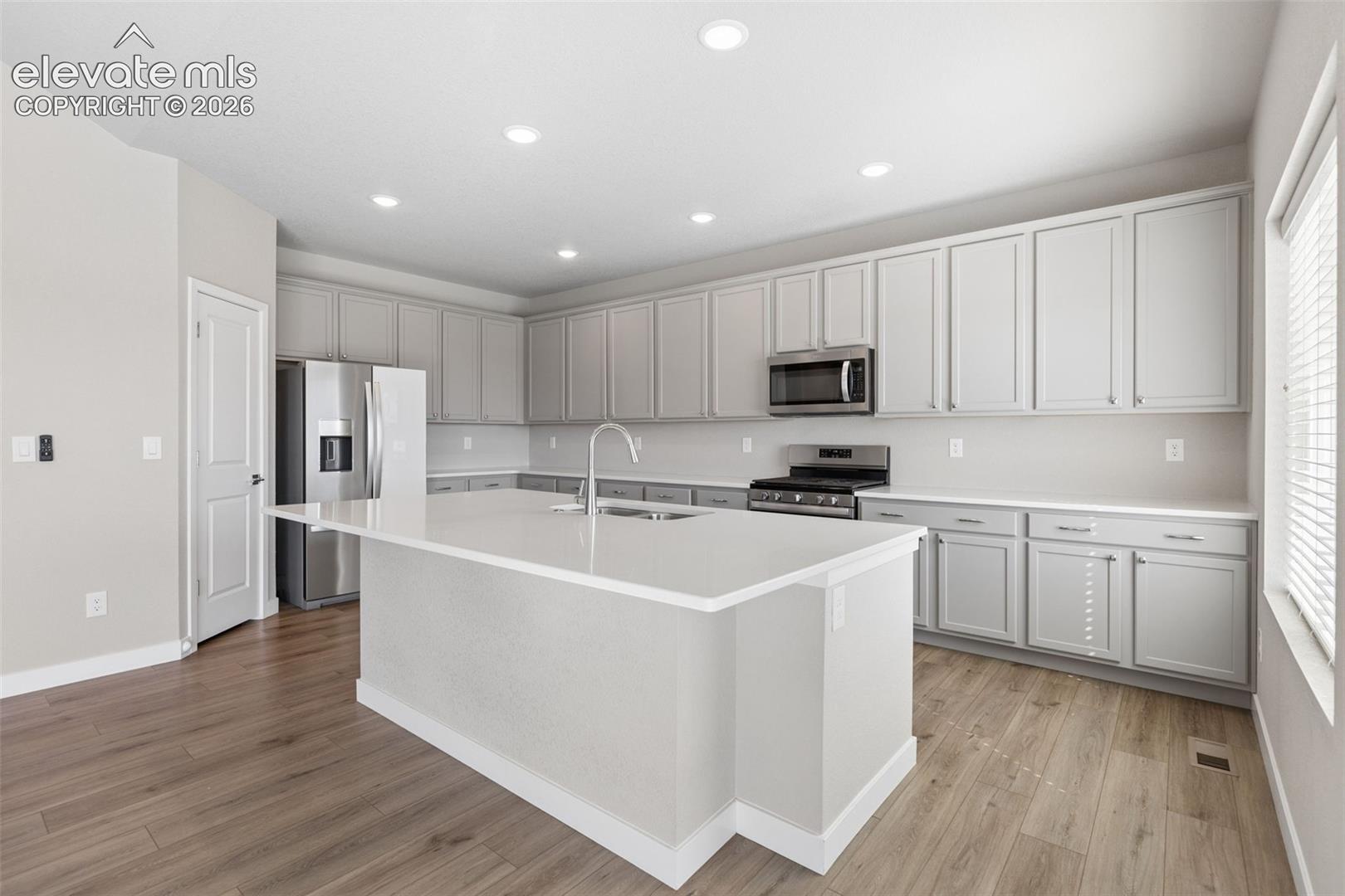 Kitchen featuring light gray cabinetry, a central island with a quartz countertop, stainless steel appliances, recessed ceiling lighting, and wood-finish flooring