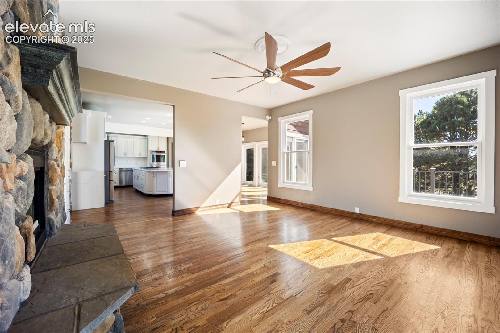 Spacious living area featuring a stone fireplace with a stone hearth, wood-finish flooring, and a ceiling fan with light fixture