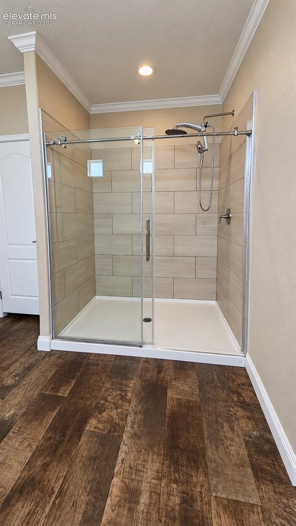 Walk-in shower featuring a glass sliding enclosure, floor-to-ceiling neutral tile surround, adjustable wall-mounted showerhead, and wood-finish flooring