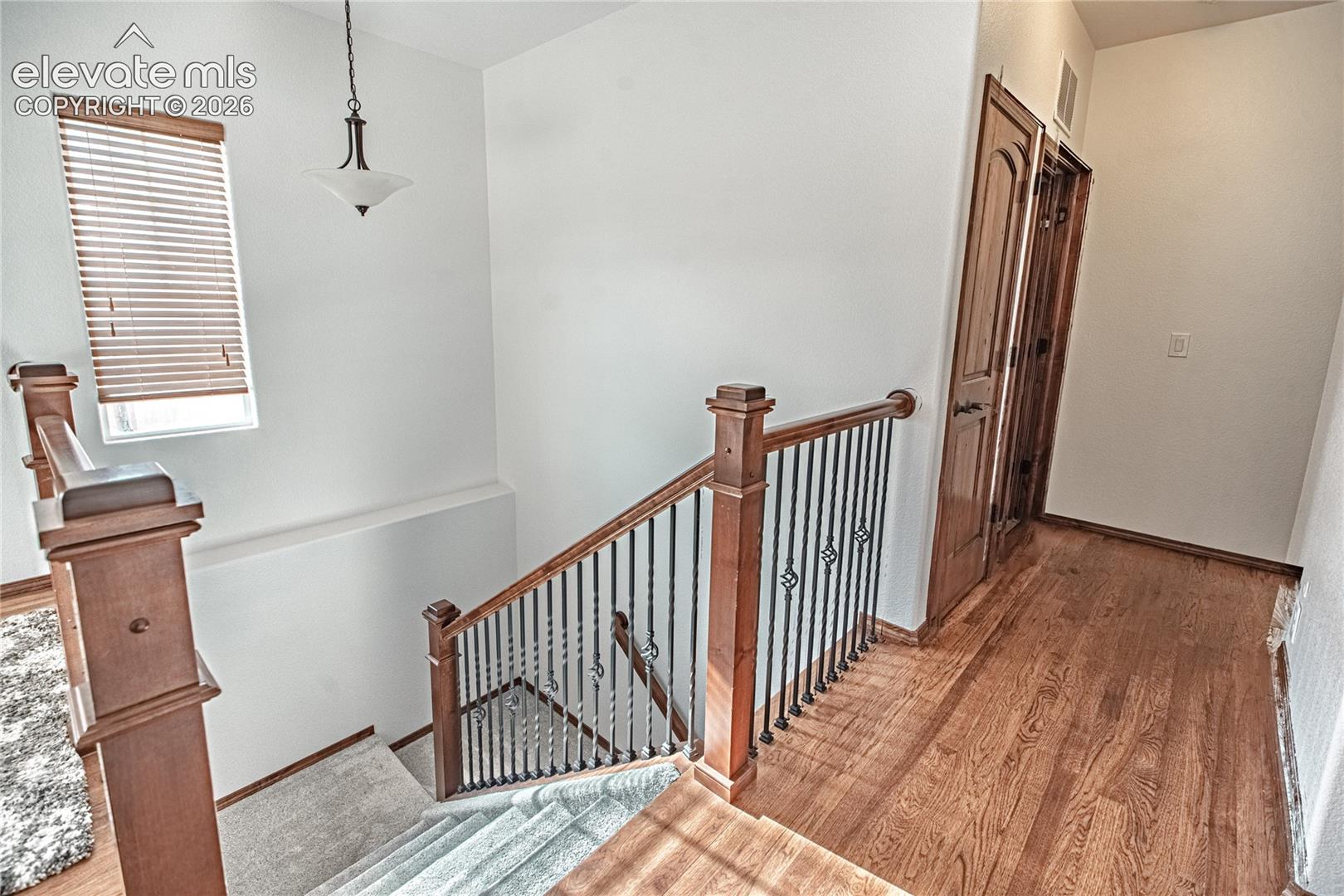 Staircase featuring wood newel posts, wrought iron balusters, and carpeted treads