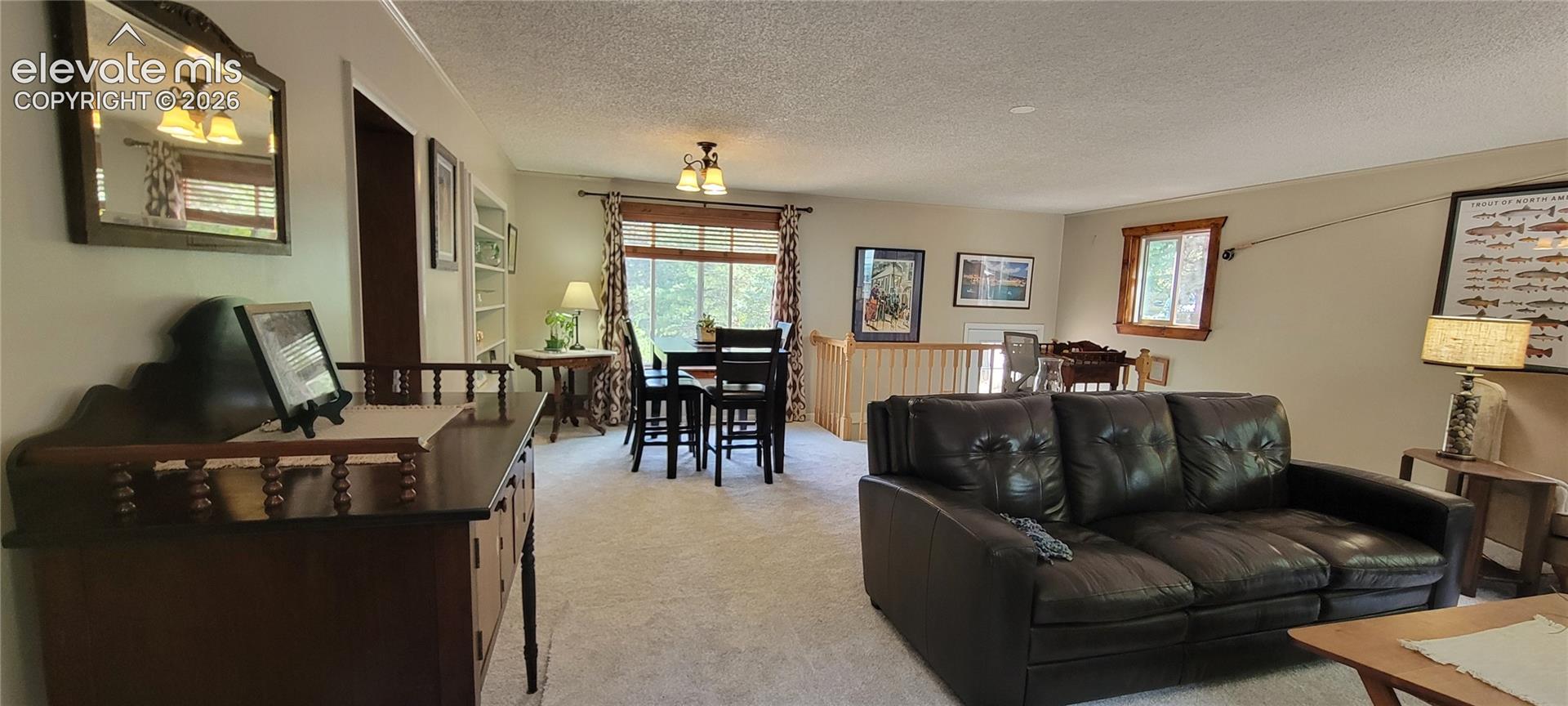 Expansive carpeted living area featuring a built-in bookshelf, a dining space with a window, and a wood railing