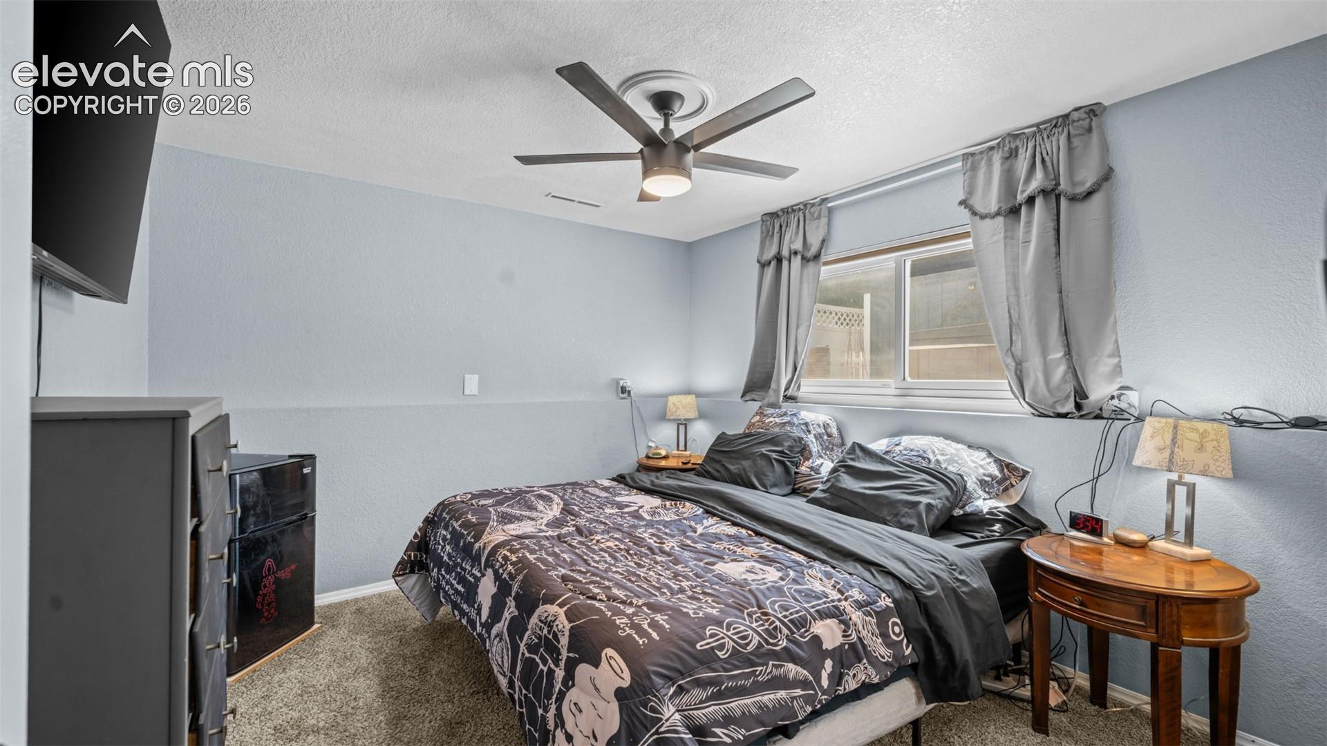 Bedroom featuring light blue walls, gray carpeting, a window with curtains, and a ceiling fan with integrated lighting