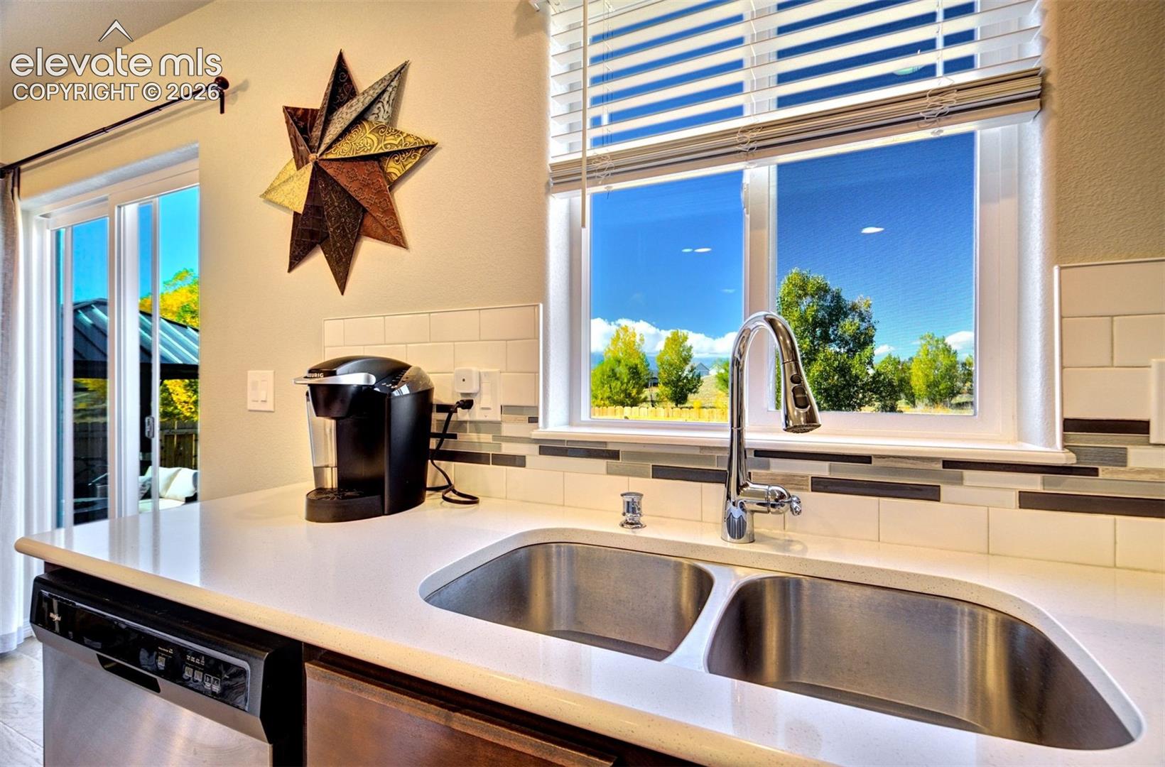 Stainless steel double-basin sink, high-arc chrome faucet, solid-surface white countertops, and horizontal subway tile backsplash