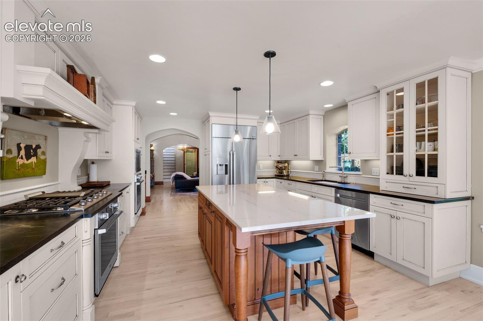 Kitchen featuring custom white cabinetry, a center island with a stone countertop, stainless steel appliances, glass-front upper cabinets, and light wood-finish flooring