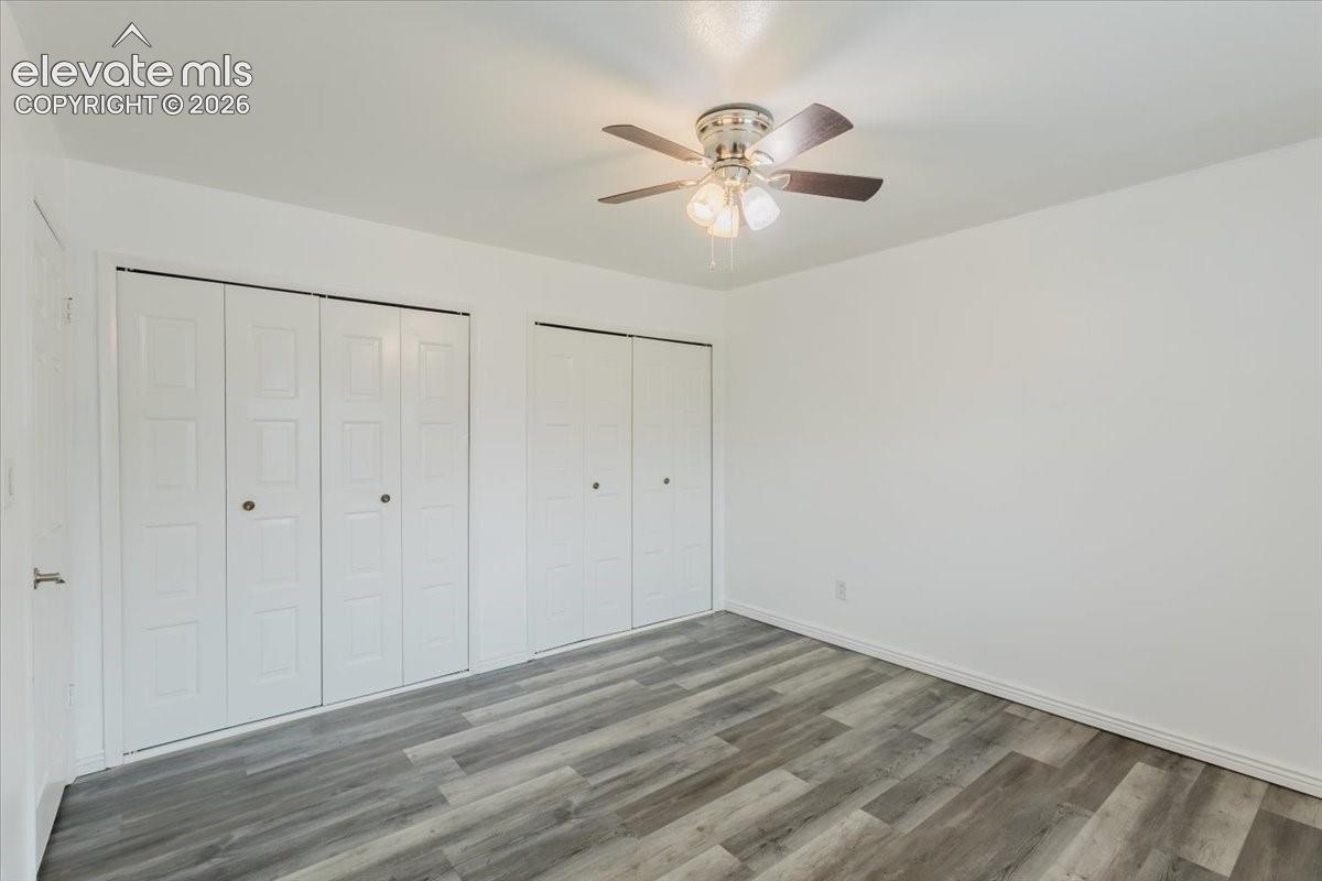 Room featuring wood-finish flooring, two sets of bi-fold closet doors, a white baseboard, and a ceiling fan with integrated lighting