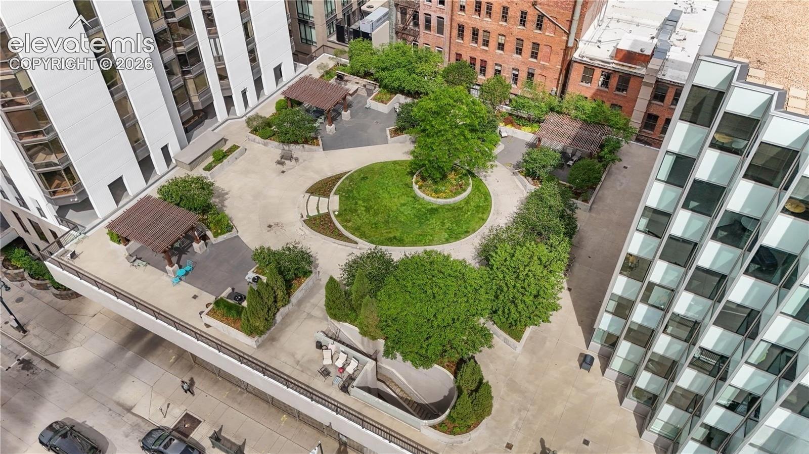 Expansive communal rooftop featuring a central circular lawn, multiple covered pergolas, paved walkways, and mature landscaping