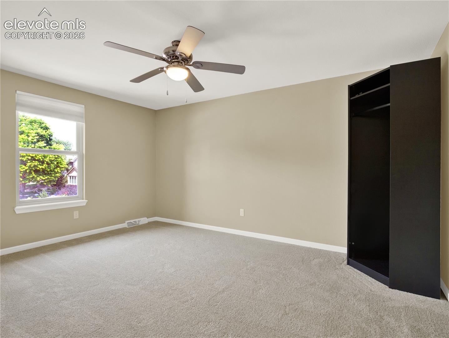 Neutral-toned interior featuring wall-to-wall carpeting, a multi-blade ceiling fan with integrated lighting, and a built-in dark finish wardrobe cabinet