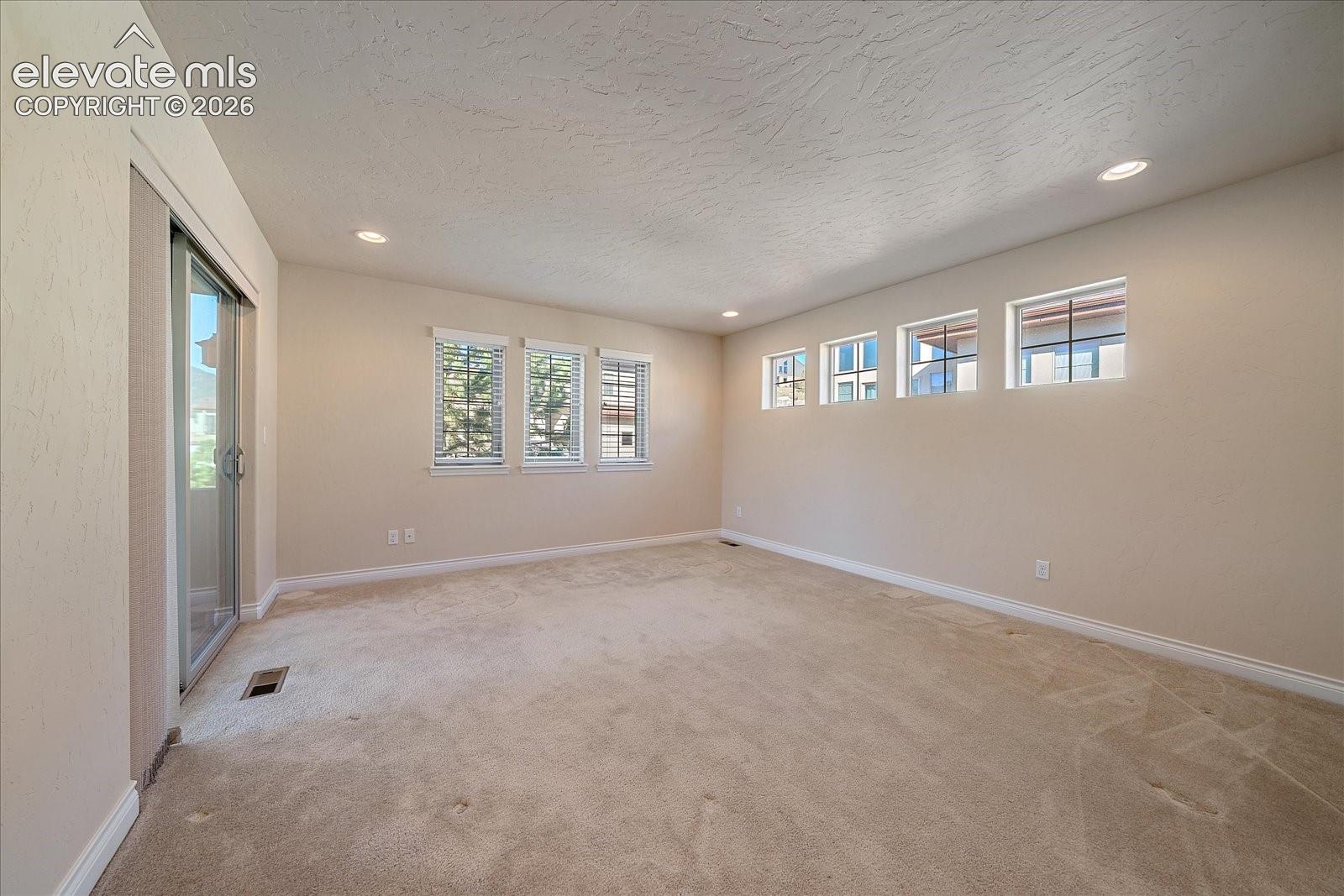 Interior space featuring neutral-toned carpeting, recessed lighting, expansive triple-pane window arrangement, supplementary clerestory windows, and a sliding glass door