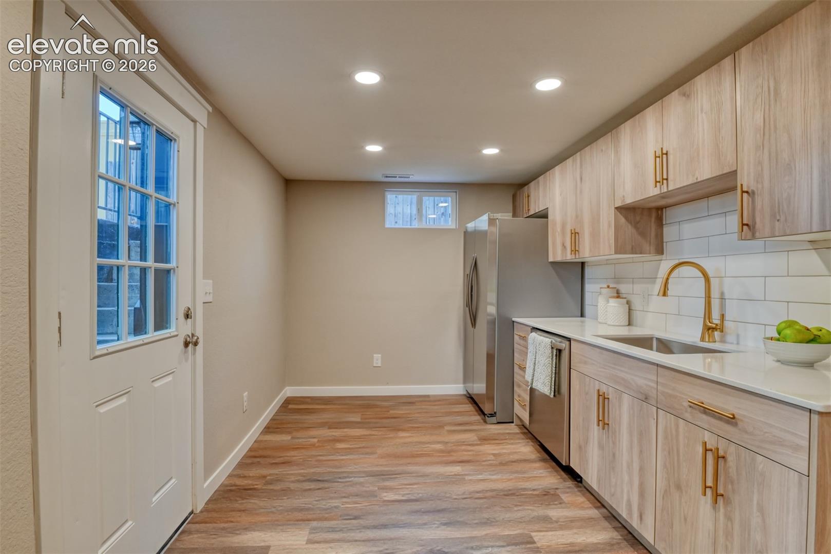 Wood-finish flooring, recessed lighting, and a kitchen featuring a stainless steel refrigerator, dishwasher, and sink with a gold-finish faucet