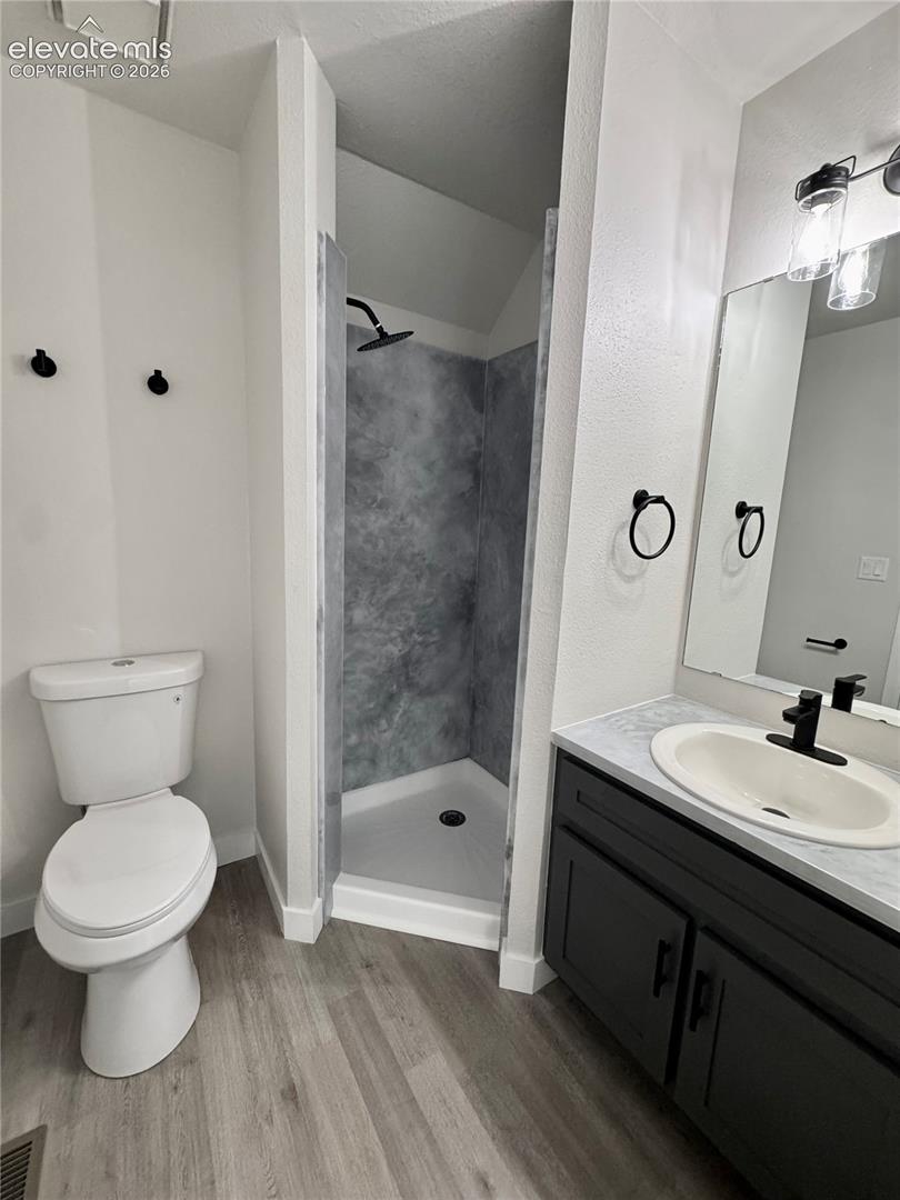 Walk-in shower with dark-toned surround, vanity with dark cabinetry, integrated sink, and wood-finish flooring
