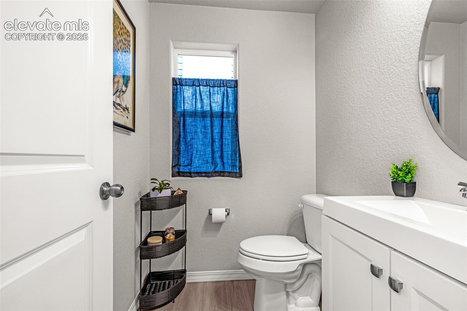 Bathroom featuring a white vanity with integrated sink, a large oval mirror, and wood-finish flooring