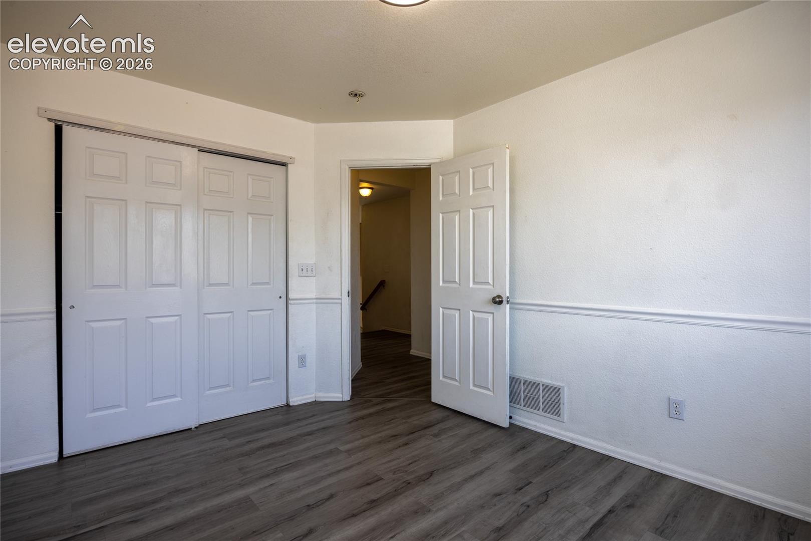 Wood-finish flooring, white paneled doors, white walls, and wainscoting