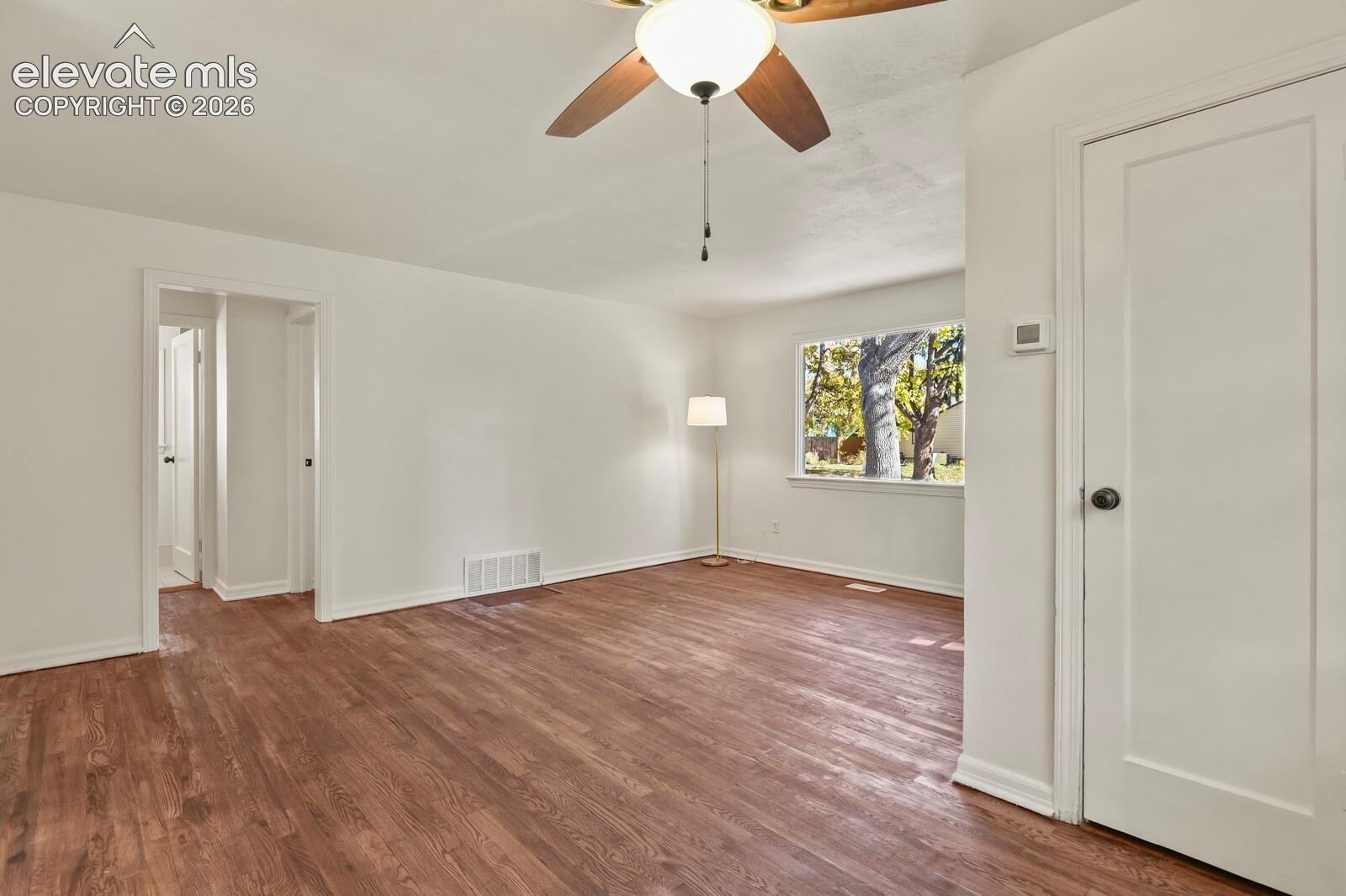 Neutral-toned interior featuring wood-finish flooring, a ceiling fan with integrated lighting, and a window with exterior greenery