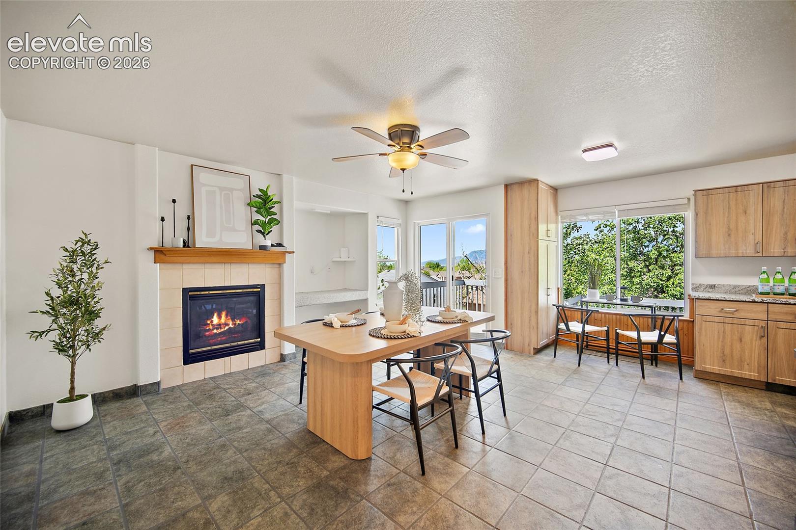 Spacious open-concept room featuring a tiled fireplace with a wood mantel, a ceiling fan, and tile flooring throughout