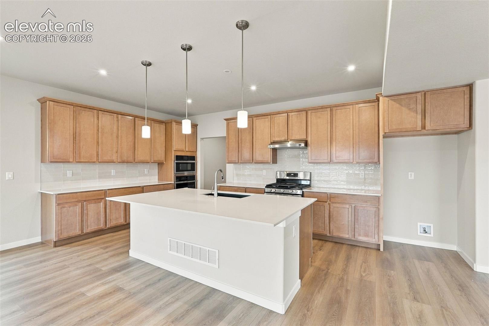 Kitchen featuring light-finish cabinetry, a center island with solid-surface countertops, recessed lighting, pendant fixtures, and wood-finish flooring