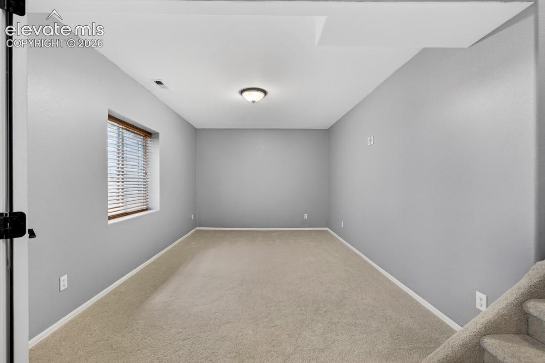 Interior room featuring neutral wall paint, wall-to-wall carpeting, recessed window with horizontal blinds, and a central ceiling-mounted light fixture