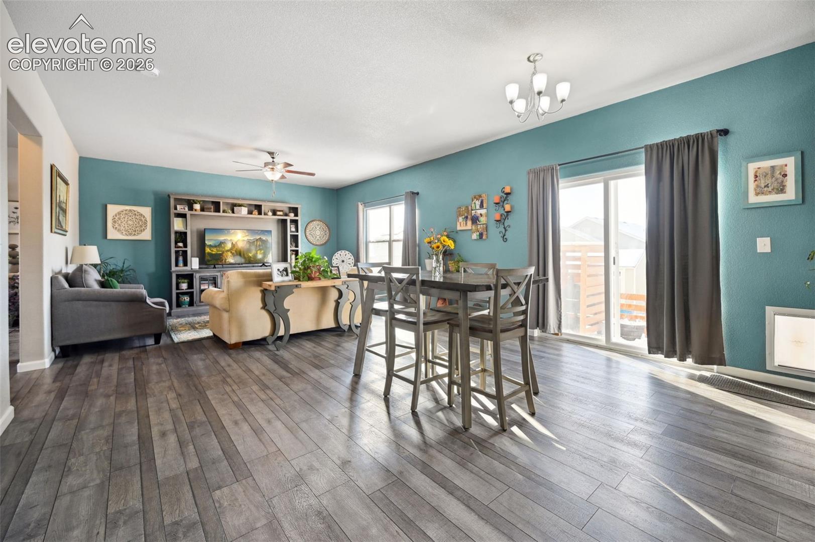 Open-concept interior featuring wood-finish flooring, built-in media cabinetry, sliding glass doors, and a multi-arm chandelier