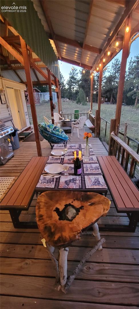 Expansive wood deck with a slatted floor, covered by a corrugated metal roof, featuring exposed wood beams and string lighting
