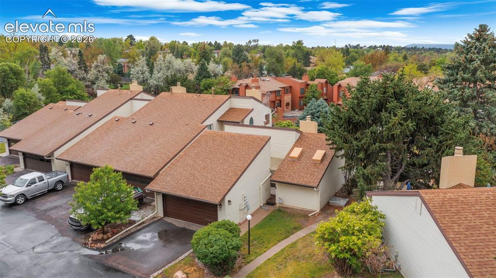 Contemporary townhome complex featuring individual garages, sloped shingle roofs, and mature surrounding trees
