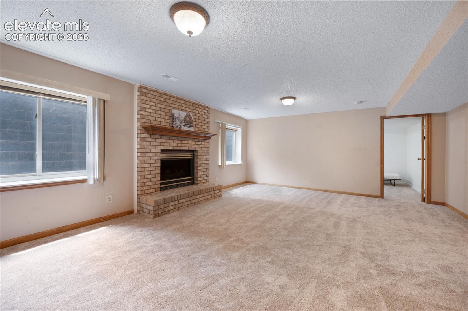 Unfurnished living room with a textured ceiling, carpet flooring, a fireplace, and baseboards
