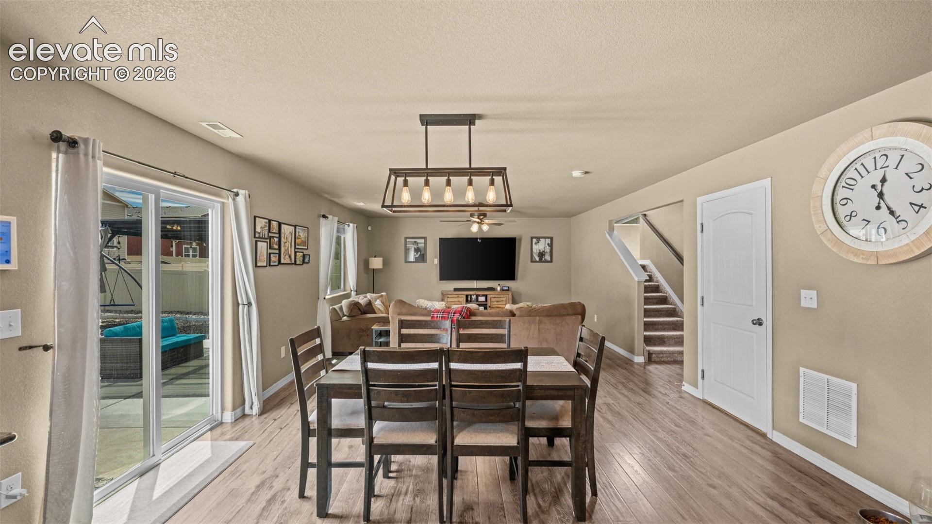 Open-concept living space featuring wood-finish flooring, a modern linear chandelier, sliding glass patio doors, a staircase with carpeted treads, and neutral wall tones