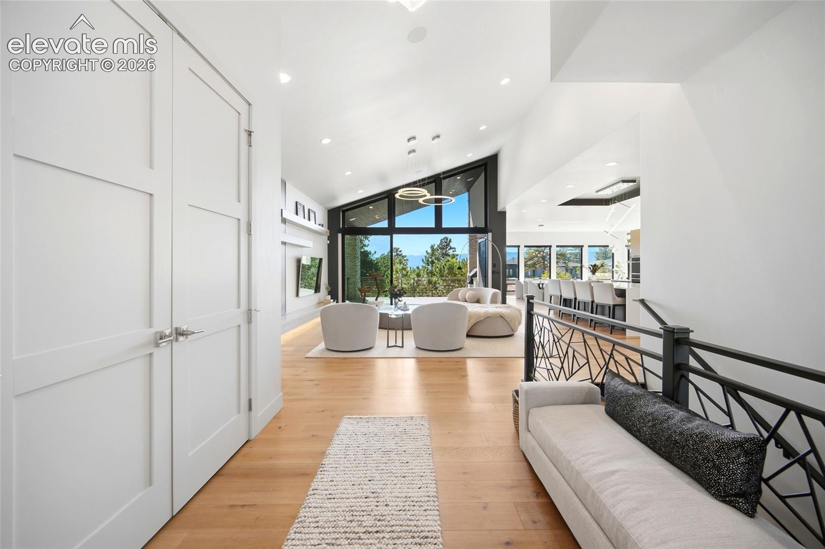 Vaulted ceilings with recessed lighting, light wood-finish flooring, and a decorative metal railing