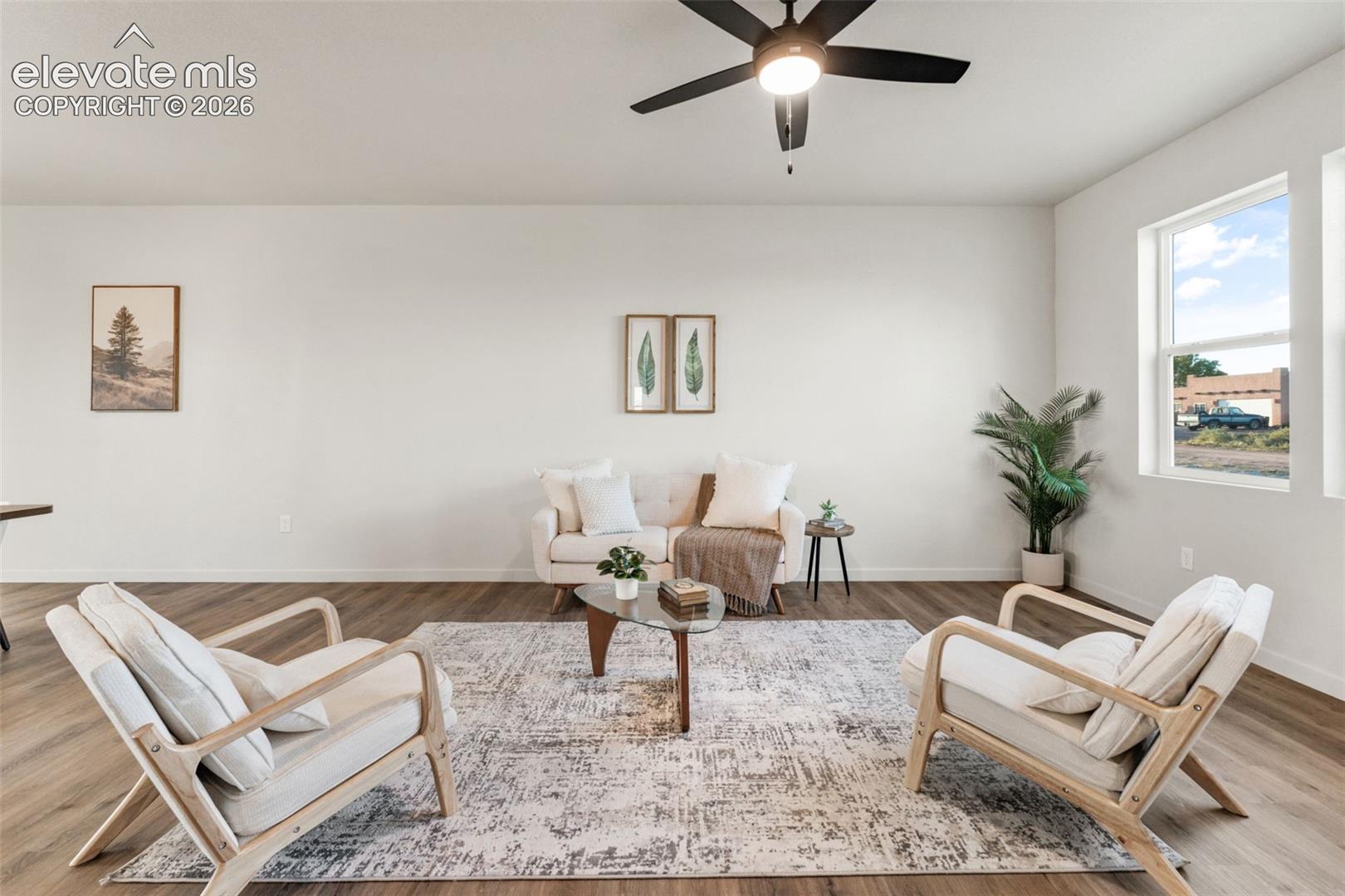 Open-concept living space featuring wood-finish flooring, high-contrast ceiling fan with integrated lighting, and neutral wall tones