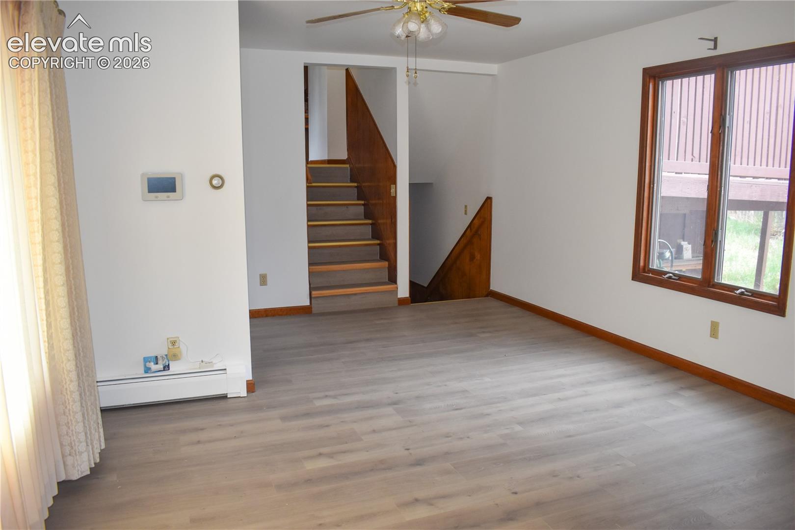 Spacious room featuring wood-finish flooring, a ceiling fan, and a large window with wood trim