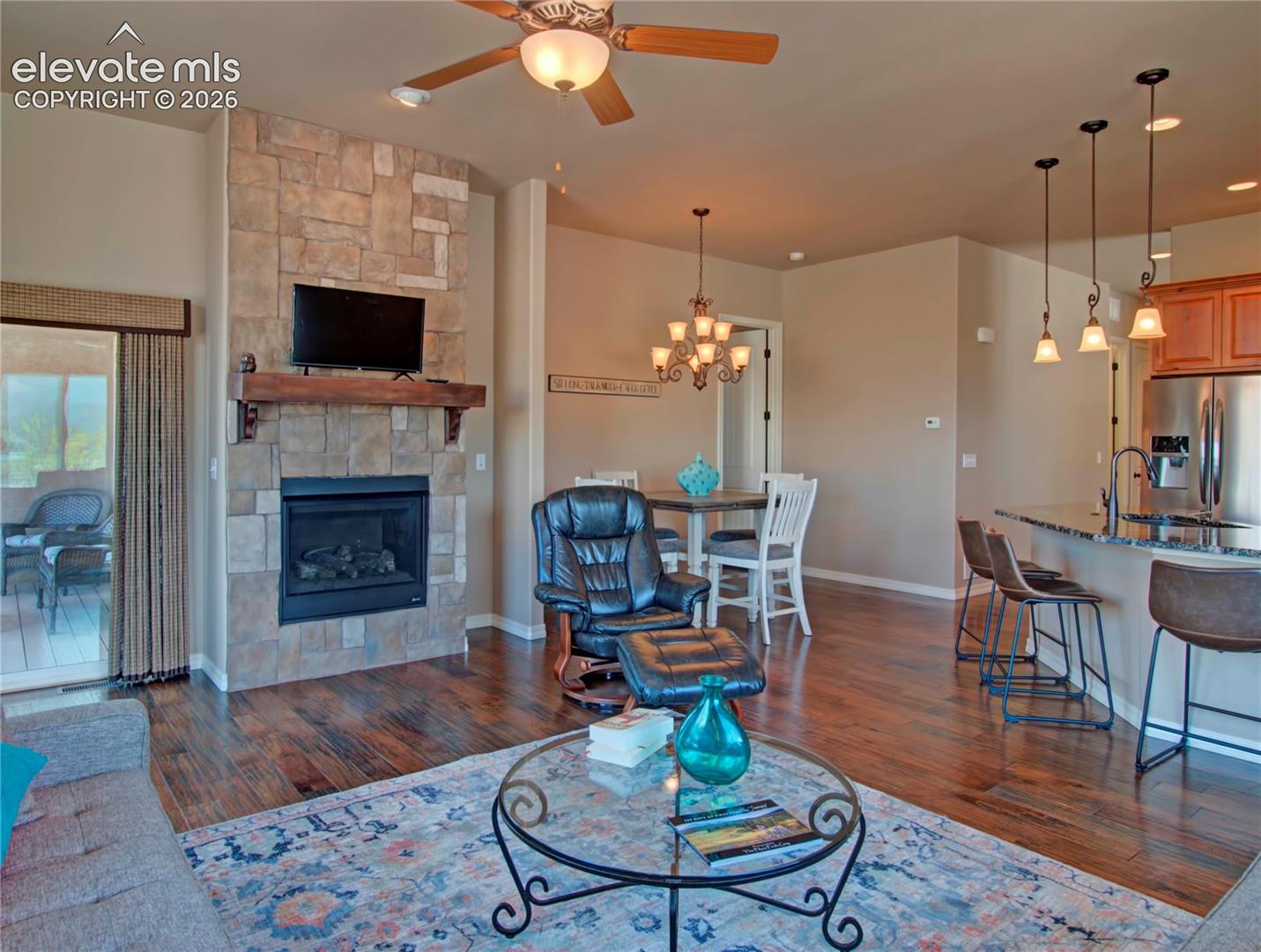 Open-concept living area with wood-finish flooring, a stone-faced fireplace, and a wood mantel