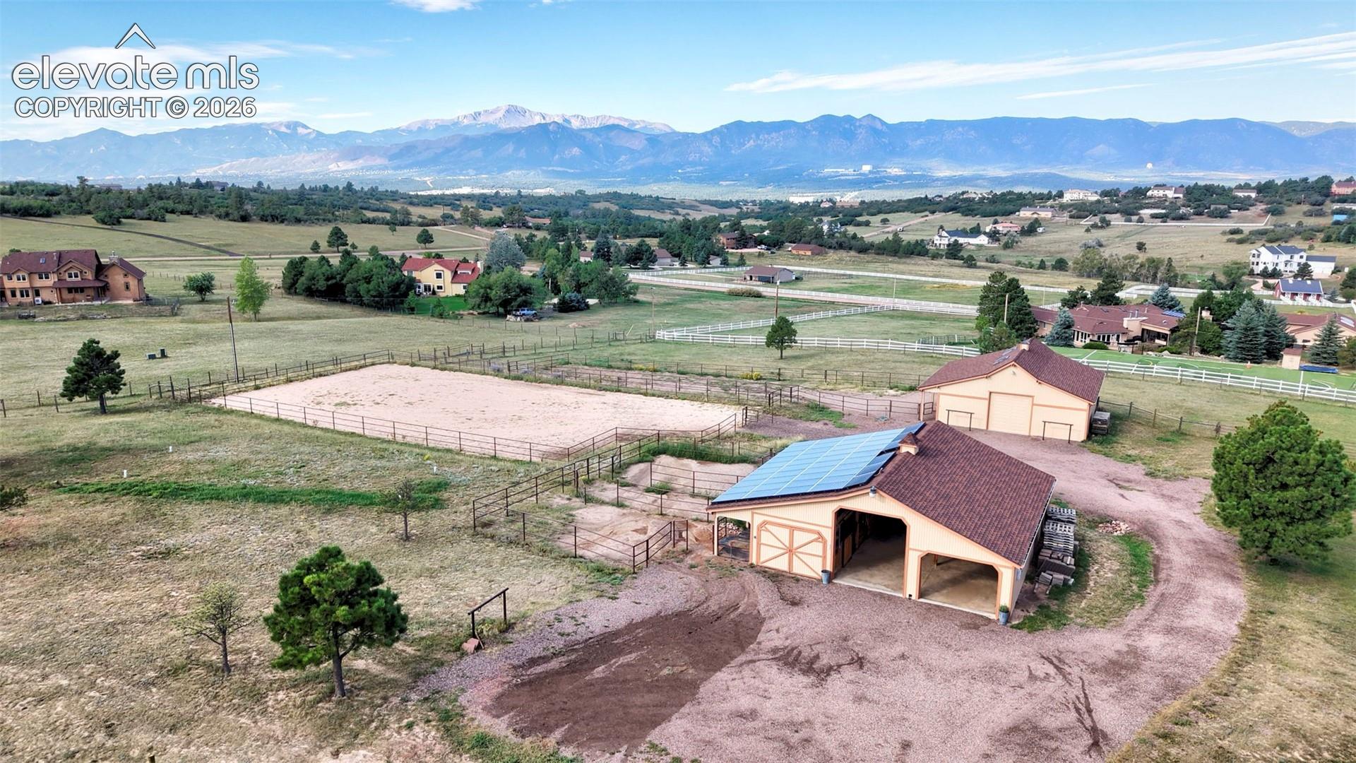 Expansive property featuring a fenced riding arena, two outbuildings with tile roofs, and solar panels.