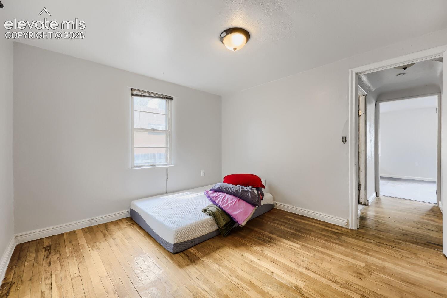 Hardwood flooring, painted walls, single window with blinds, overhead light fixture, and an open doorway