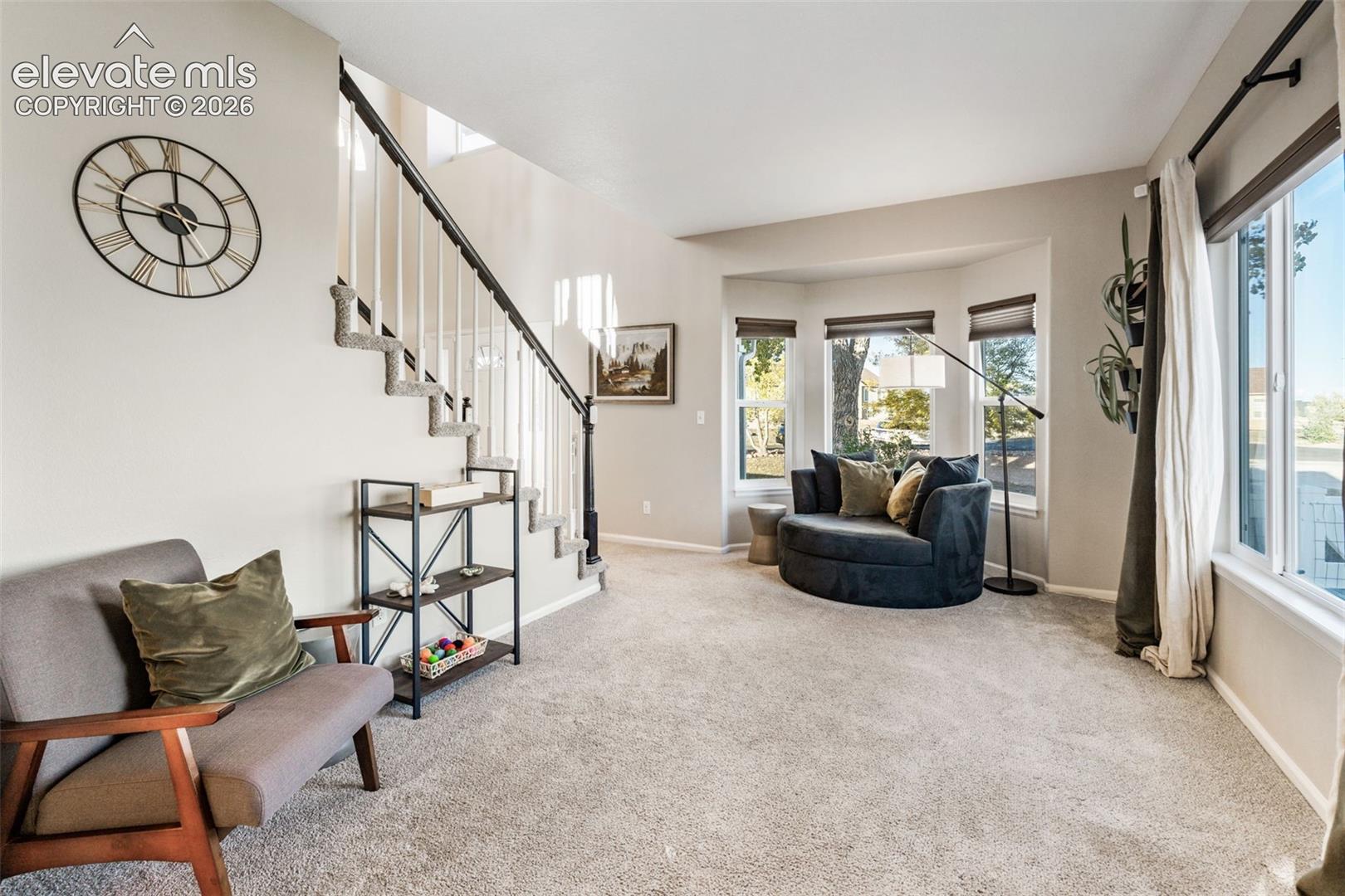 Staircase featuring a black metal railing with white balusters, expansive bay window, and carpeted flooring