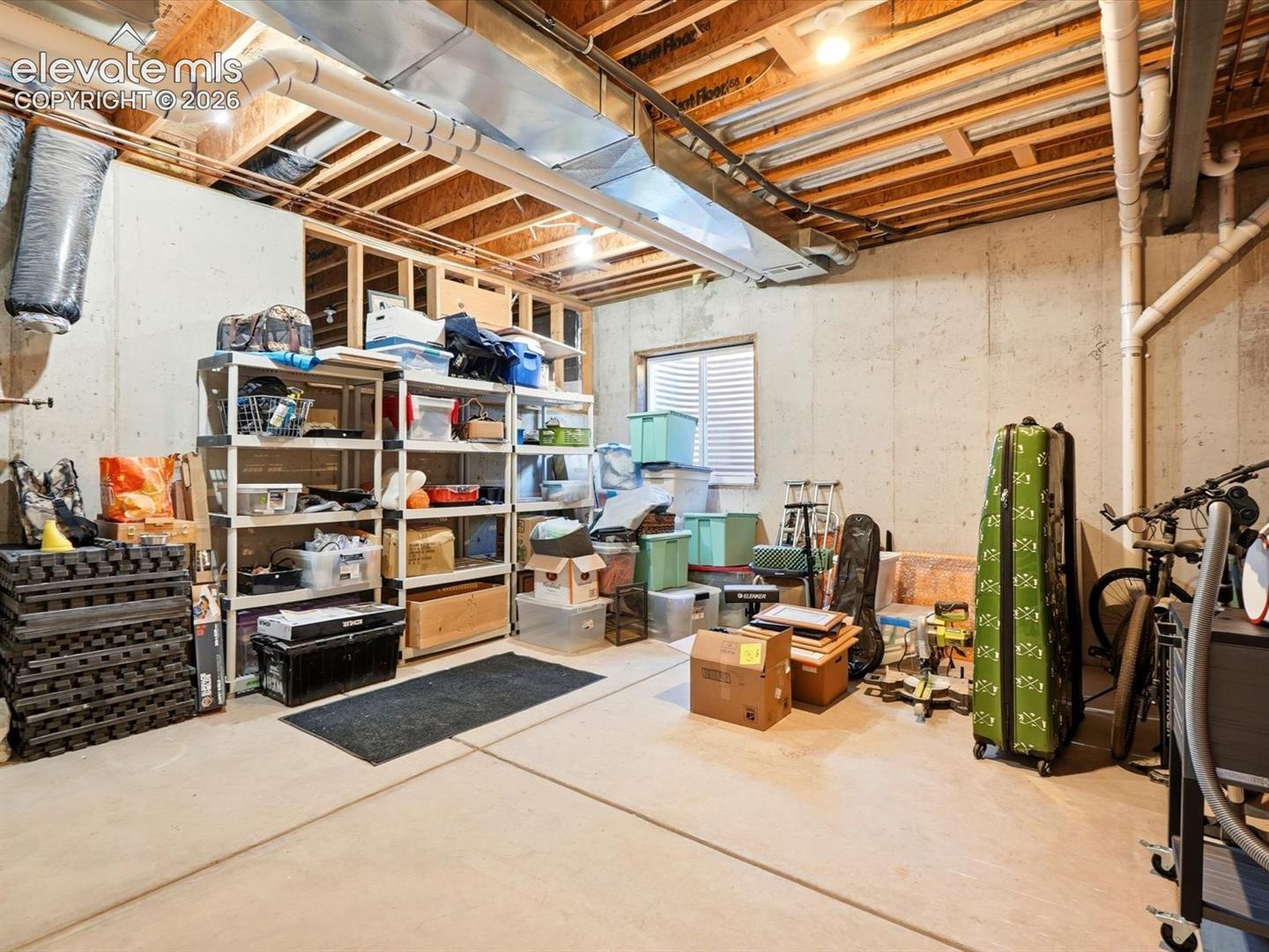 Unfinished storage area featuring concrete foundation walls, exposed wood-joist ceiling, concrete flooring, and a single egress window