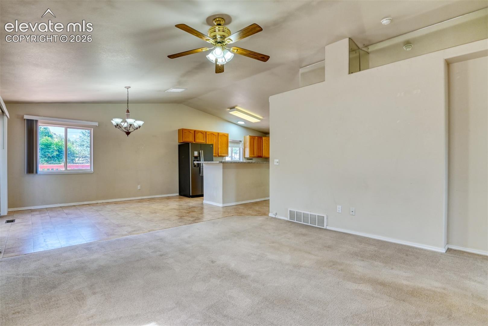 Vaulted ceiling with a centrally mounted ceiling fan, tile flooring, kitchen featuring wood cabinetry and a breakfast bar, and an installed multi-light chandelier