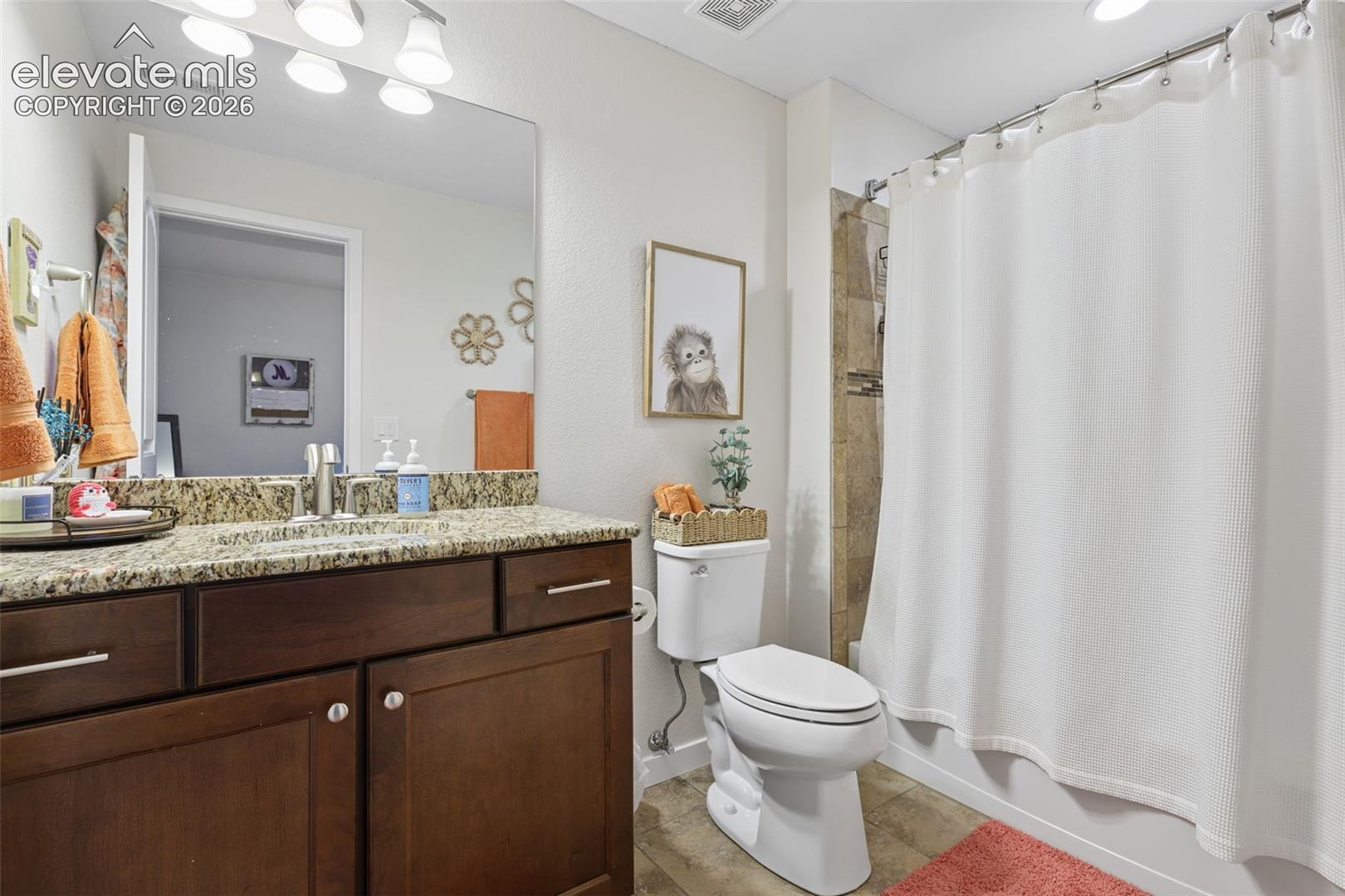 Vanity with granite-style countertop, undermount sink, and wood-finish cabinetry, alongside a tiled shower enclosure