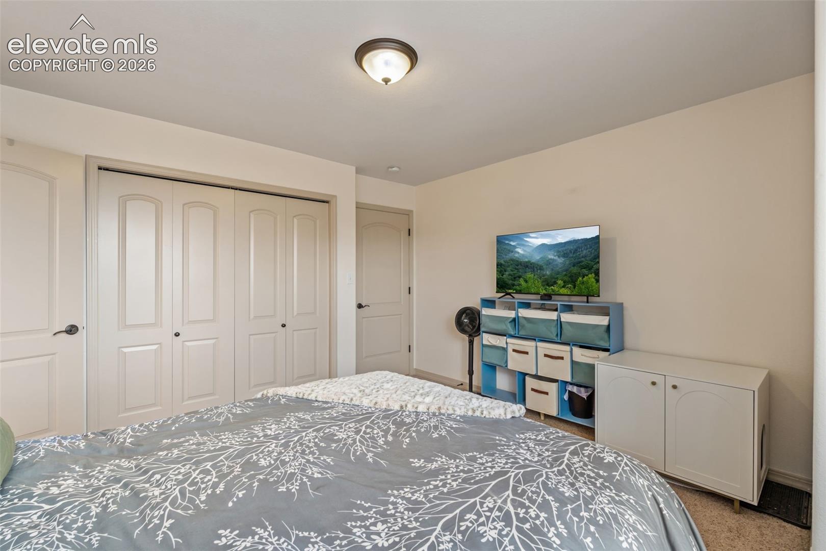 Bedroom featuring a flush-mount ceiling light, light beige wall paint, and white bi-fold closet doors with black hardware