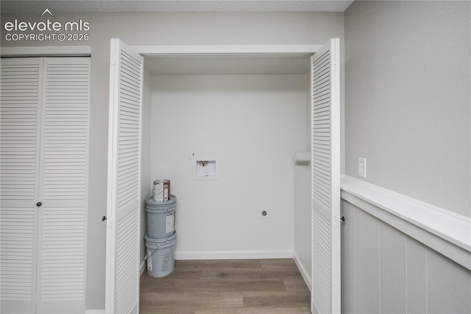 Laundry utility area featuring louvered bifold doors and wood-finish flooring