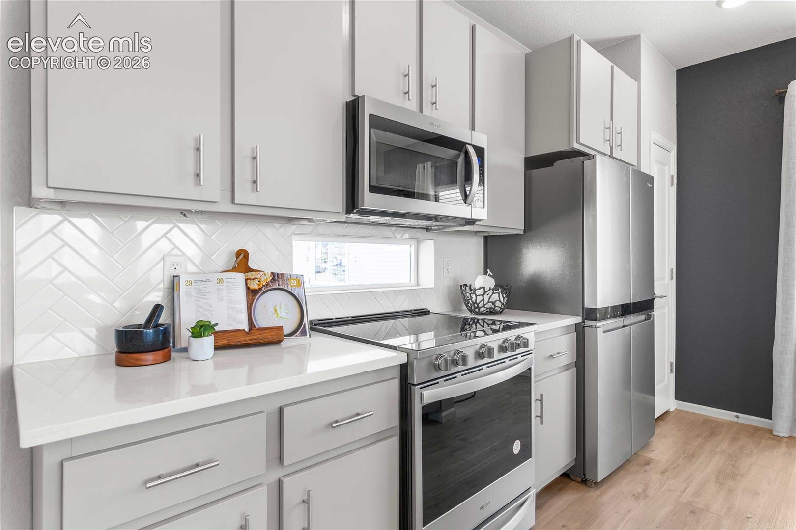 Kitchen featuring light-toned cabinetry, stainless steel appliances, white herringbone tile backsplash, light-toned countertops, and wood-finish flooring
*photos of a model home*